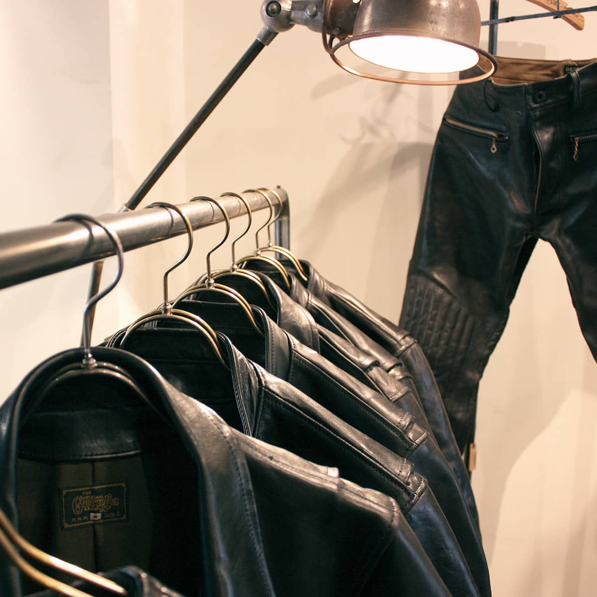 GANZ定番の黒皮鉄製ハンガーラック(店舗什器)とレザージャケット・レザーパンツのディスプレイ。